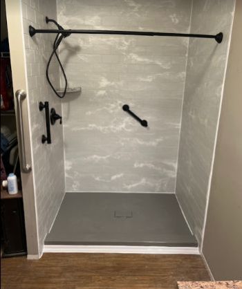 Walk-in tiled shower stall with black grab bars, shower head, and gray pan floor